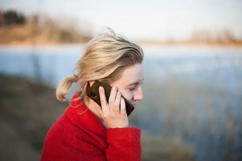 Eine Frau in roter Jacke telefoniert im Freien und hört aufmerksam zu.