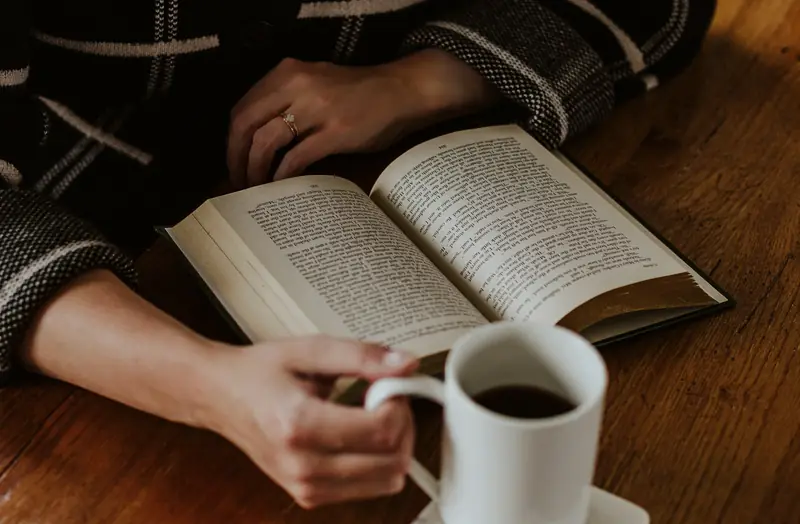 Eine Person hält ein Buch, daneben eine Tasse Kaffee.