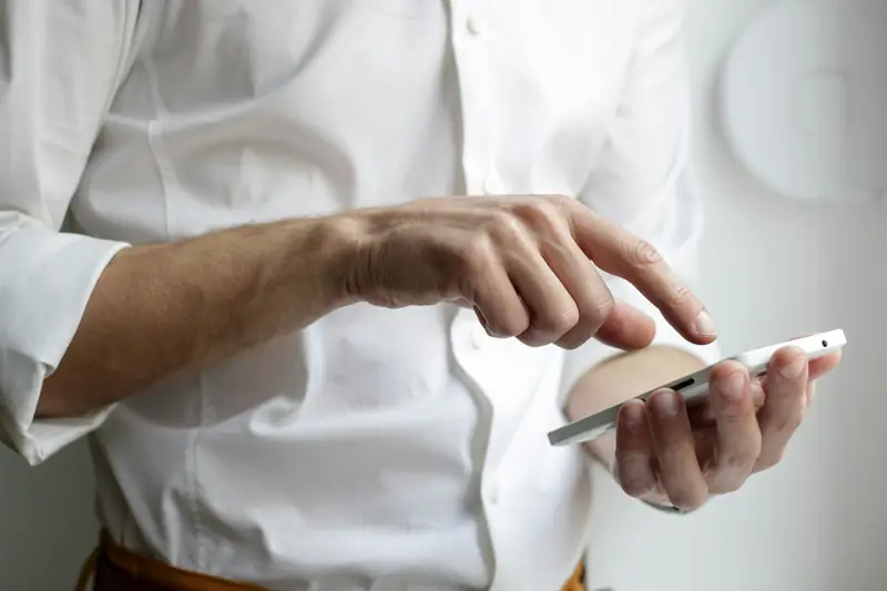 Ein Mann im weissen Hemd tippt mit dem Finger auf sein Smartphone.