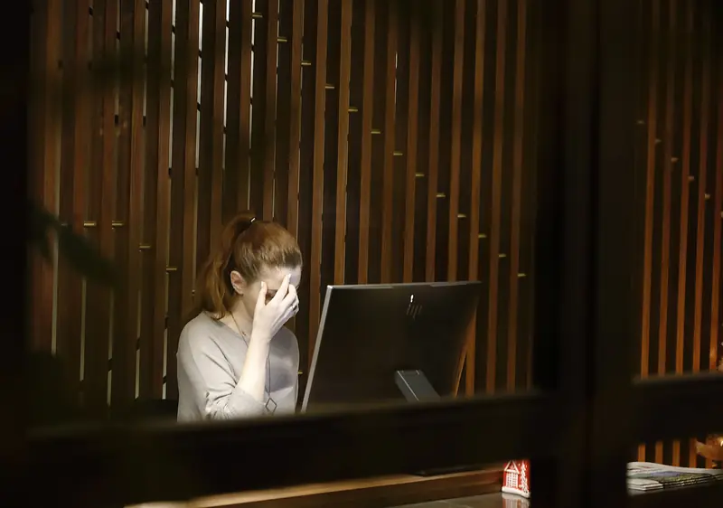 Eine Frau sitzt vor einem Computer und hält die Hand an die Stirn.