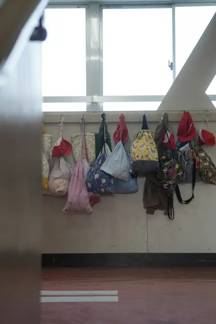 Bunte Taschen und Hüte hängen an Garderobenhaken in einem Schulgang.