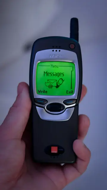 Eine Hand hält ein altes Tastenhandy mit einer neuen Nachricht auf dem grünen Display.