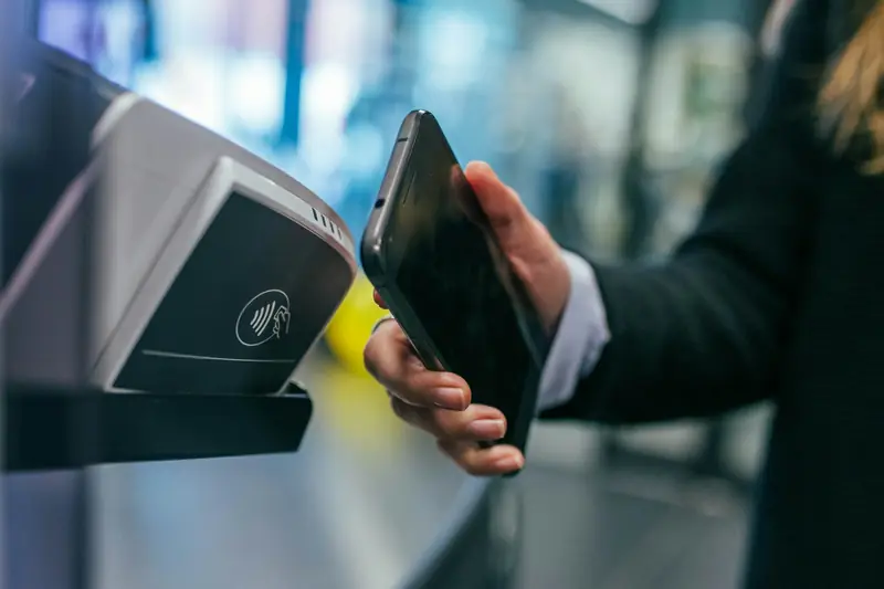 Eine Hand hält ein Telefon an ein Zahlterminal.