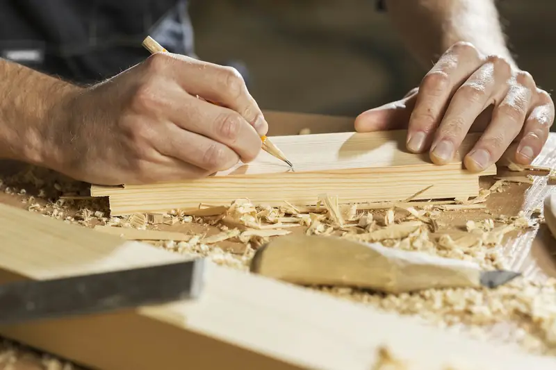 Eine Hand zieht mit dem Bleistift eine Linie auf einem Holzbrett.