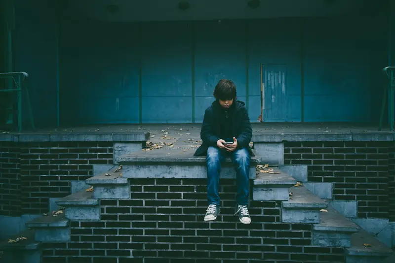 Ein Jugendlicher sitzt allein auf einer Treppe und schaut auf sein Telefon.