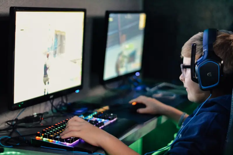 Ein Junge mit Headset spielt an einem Computer mit zwei Bildschirmen.