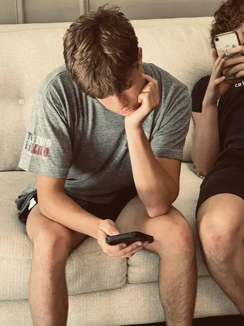 Zwei Jugendliche sitzen auf einem Sofa, jeder schaut auf sein eigenes Telefon.