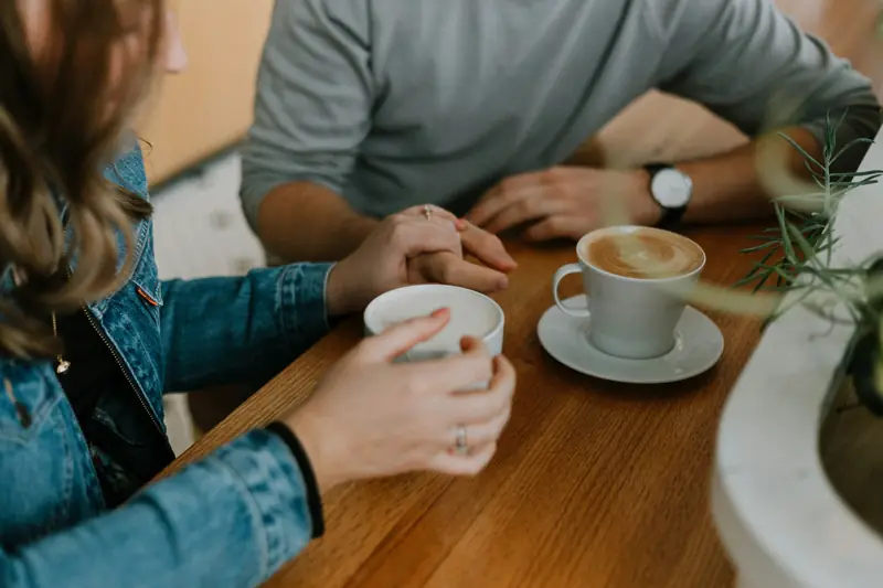 Zwei Menschen sitzen an einem Holztisch, vor ihnen zwei Tassen Kaffee.
