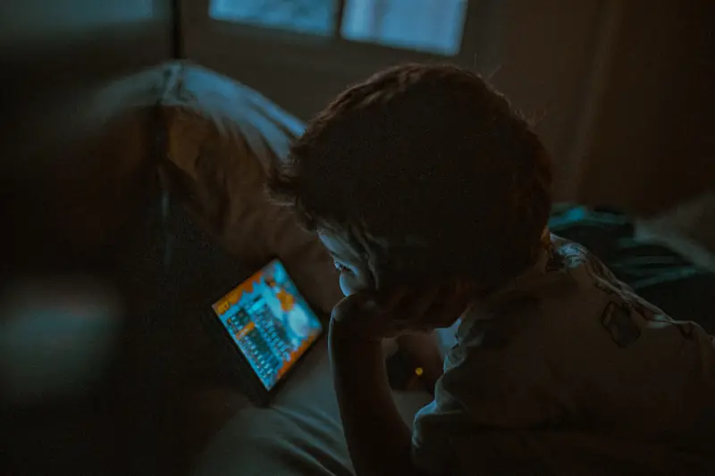 Ein Kind schaut in einem dunklen Raum auf ein Tablet.