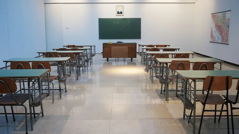 Ein leeres, helles Klassenzimmer mit Pulten und einer grünen Wandtafel.