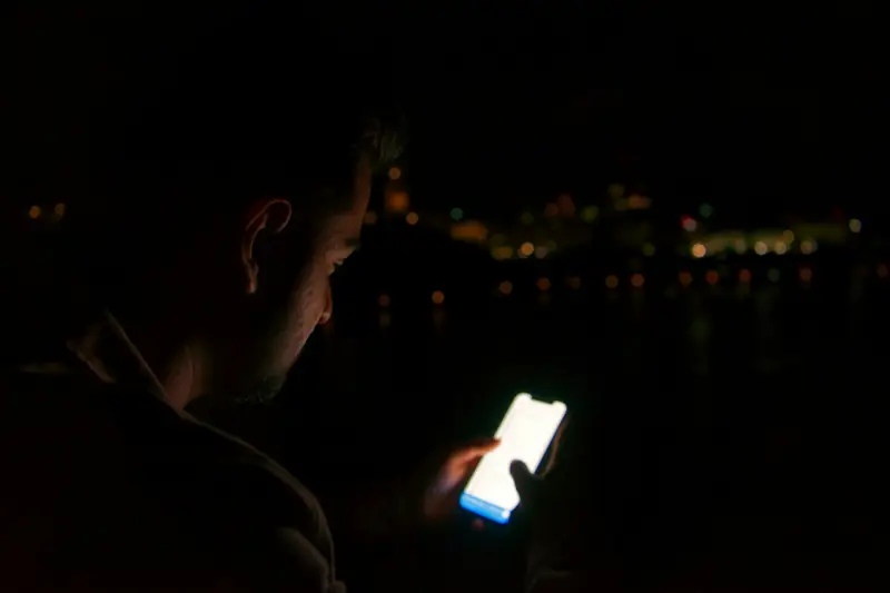 Ein Mann schaut nachts auf das Licht seines Telefons.