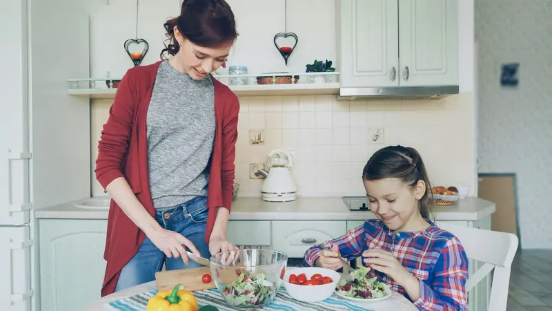 Eine Mutter und ihre Tochter bereiten in der Küche gemeinsam einen Salat zu.