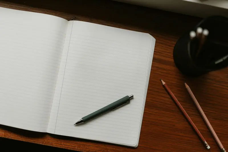 Ein offenes, leeres Notizbuch mit Stiften auf einem Schreibtisch.