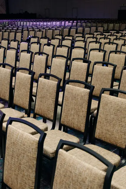 Reihen leerer Stühle in einem hellen Saal, bereit für einen Abend.