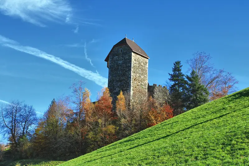 Ein steinerner Turm auf einem Hügel zwischen Herbstbäumen bei Wattwil.